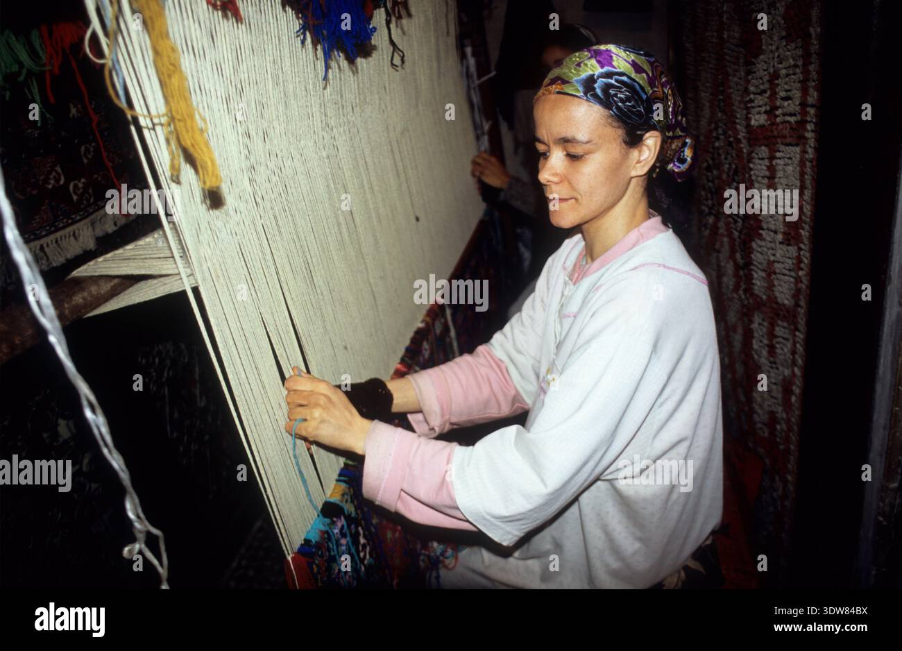 Eine Handwerkerin fädelt Wollgarn manuell auf einem großen vertikalen Webstuhl, um einen traditionellen Teppich in einer Werkstatt in Fès, Marokko, zu weben. Stockfoto