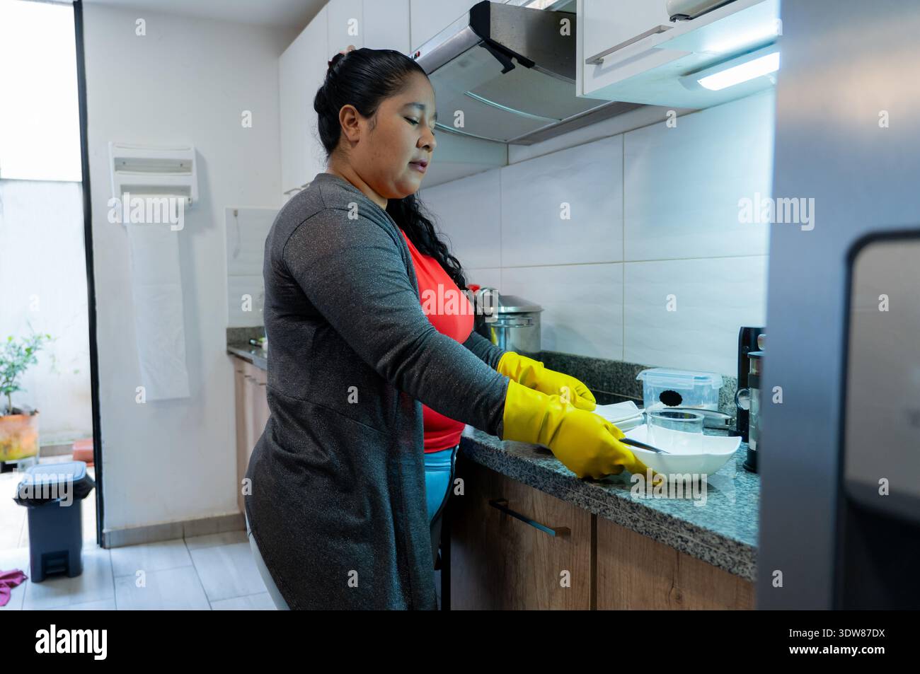 Frau, die gelbe Gummihandschuhe trägt, Geschirr in einer Küche zu reinigen Stockfoto