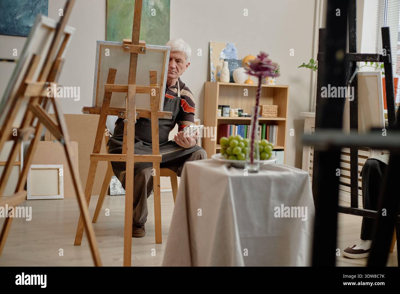 Ältere kaukasische Männermalerei auf Leinwand während des Kunstkurses in pädagogischem Umfeld Stockfoto