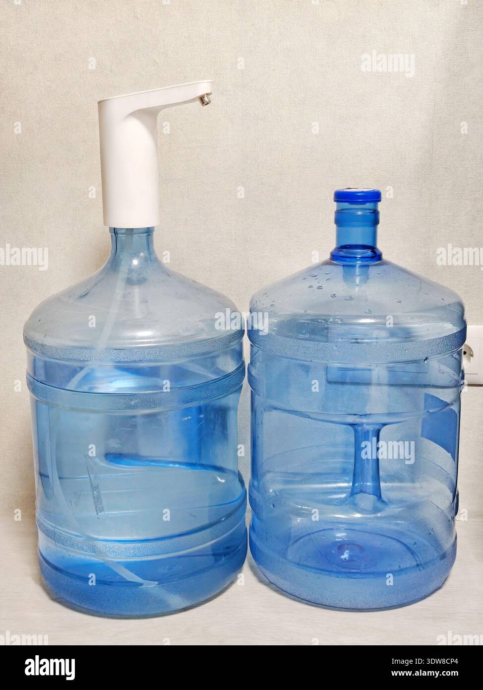 Zwei große blaue Wasserflaschen stehen nebeneinander, eine mit einer elektrischen Wasserpumpe oben. Klare Kunststoffbehälter für Trinkwasser, platziert i Stockfoto