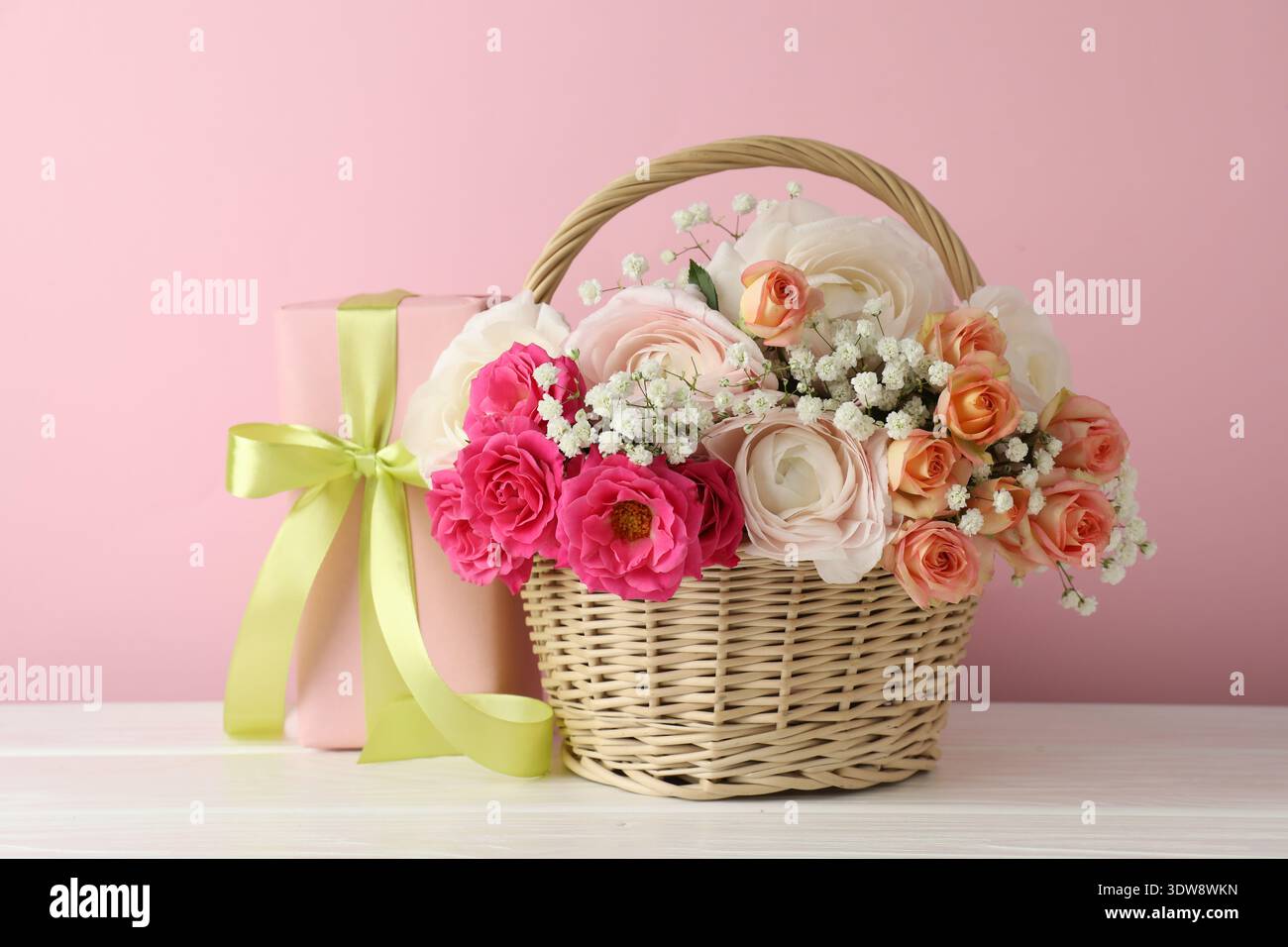 Schöne Blumen im Korb und Geschenk auf weißem Holztisch Stockfoto