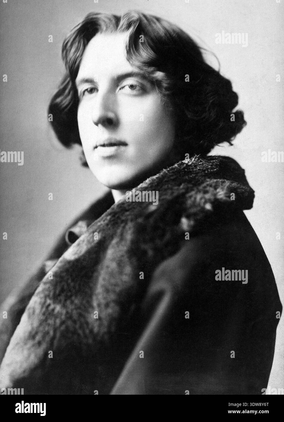 Dieses auffällige Schwarz-weiß-Porträt von Oscar Wilde, das um 1882 vom renommierten Fotografen Napoleon Sarony aufgenommen wurde, zeigt das unverwechselbare Aussehen und die künstlerische Persönlichkeit des irischen Schriftstellers. Wilde trägt einen Mantel mit Pelzkragen, seine lockigen Haare und sein nachdenklicher Blick, der zum ikonischen Bild der gefeierten Literaturfigur während der ästhetischen Bewegung beiträgt. Stockfoto