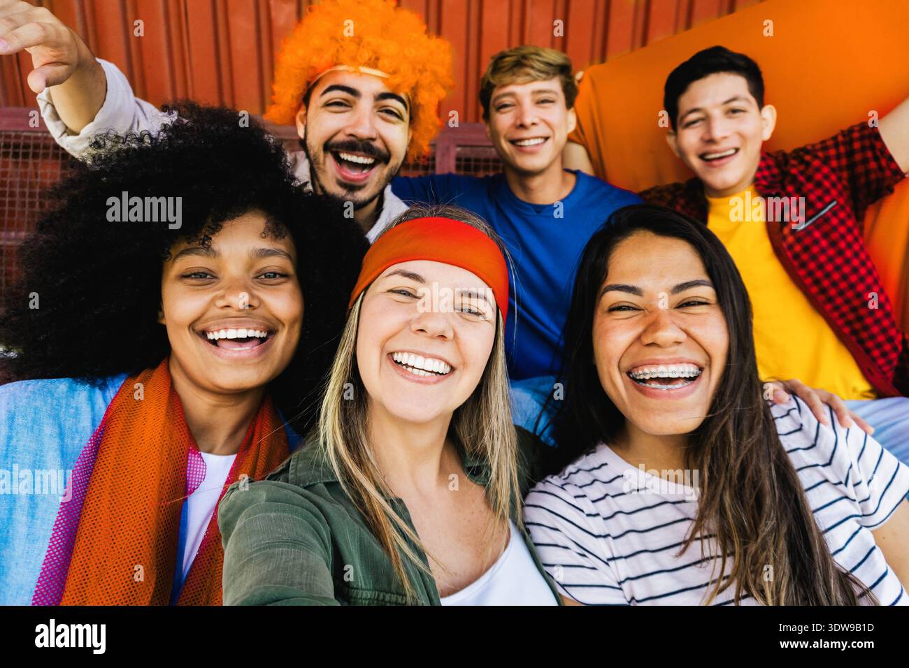 Orangene Fußballfans jubeln im Stadion an – Fans aus mehreren Rassen feiern internationales Meisterschaftsspiel Stockfoto