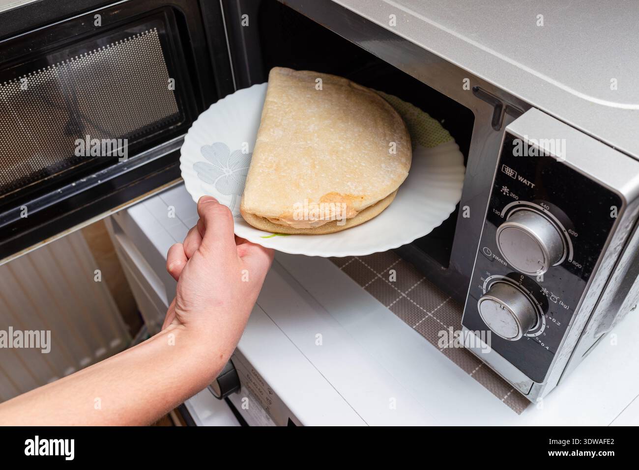 Ungesundes Essen, Fast Food, Junk Food Konzept. Unverarbeitete Fast Food ungesunde kleine gefrorene Pizza in die Hand des Jungen gelegt, während sie in die Mikrowelle gelegt wird. Stockfoto