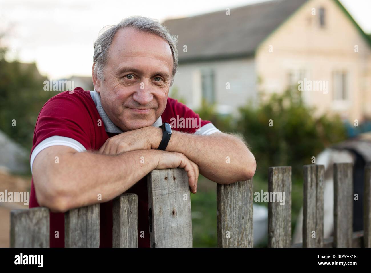 Ein älterer Mann steht neben einem Holzzaun im Gemüsegarten Stockfoto