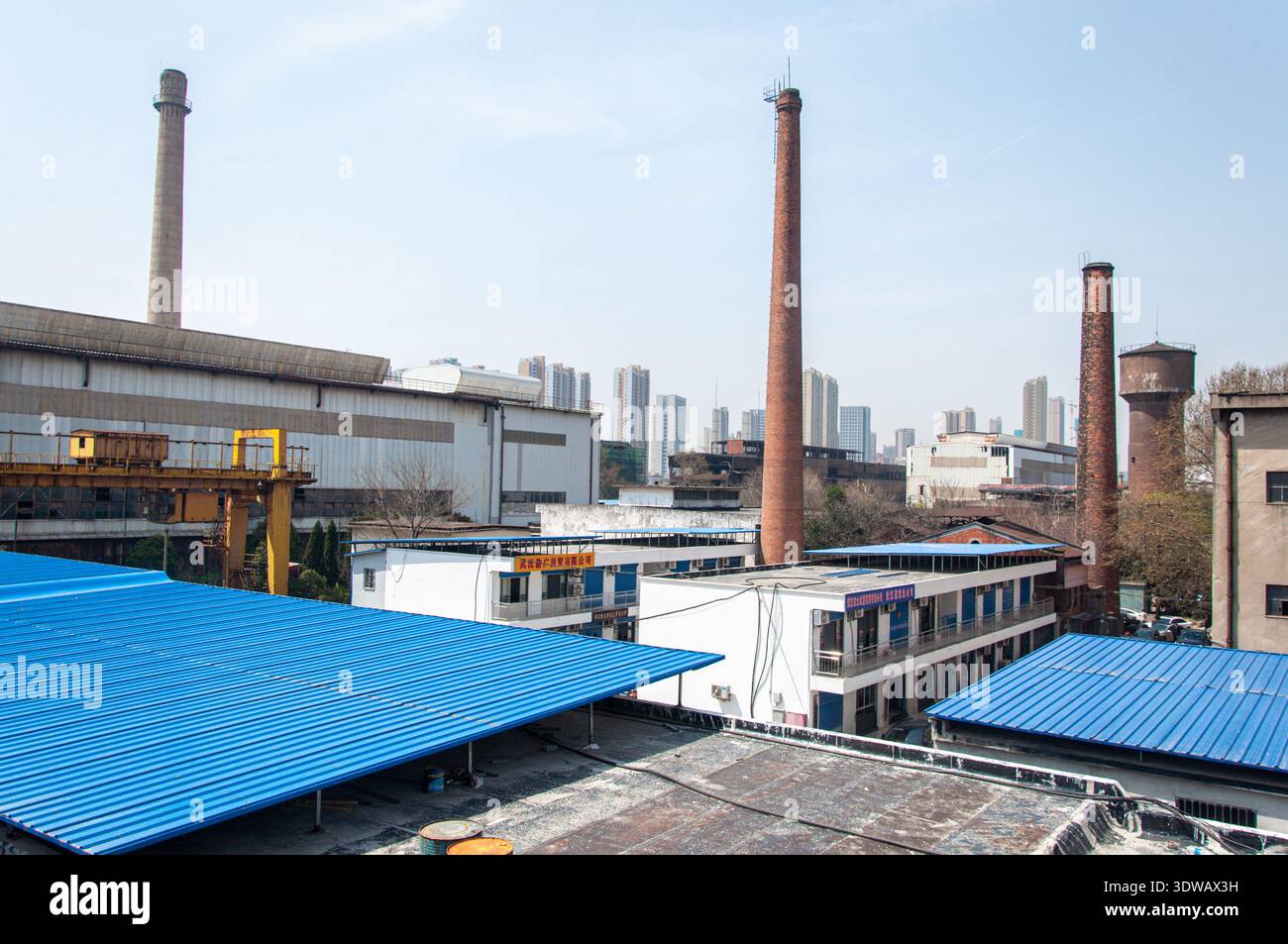Wuhan, Provinz Hubei, China - 23. März 2018: Hohe industrielle Schornsteine erheben sich über den blau-weißen Dächern alter Fabrikgebäude Stockfoto