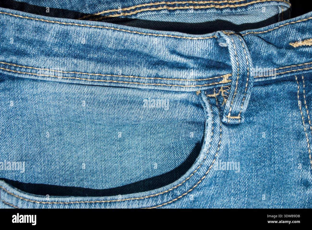 Nahaufnahme von blauen Denimjeans, die die Vordertasche, den Gürtelschlitz, den Bund und die gelbe Nähstruktur zeigen. Stockfoto