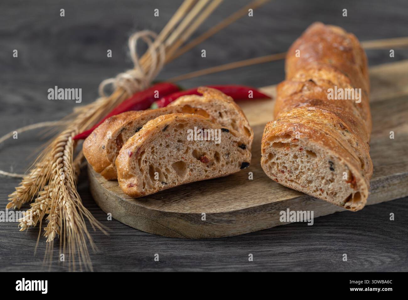 In Scheiben geschnittenes Roggenweizen-Baguette mit Kleie und Peperoni auf einem Holzbrett. Stockfoto