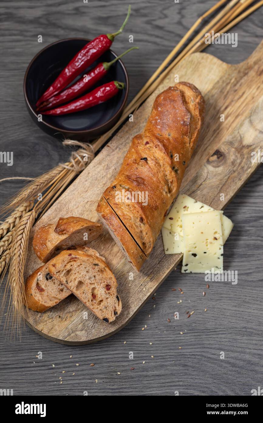 In Scheiben geschnittenes Roggenweizen-Baguette mit Kleie und Peperoni auf Holzbrett. Stockfoto