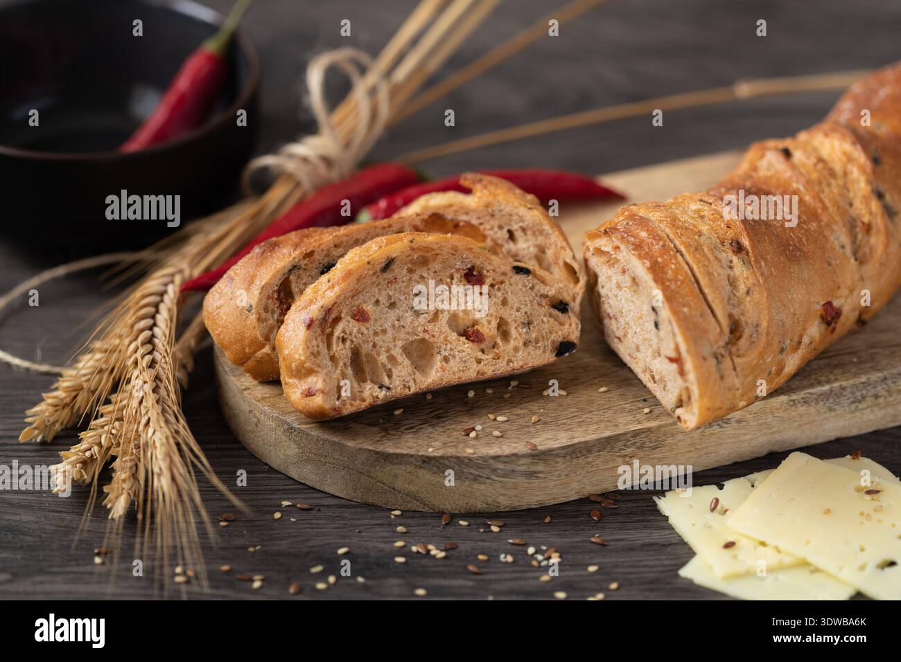 In Scheiben geschnittenes Roggenweizen-Baguette mit Kleie und Peperoni auf einem Holzbrett. Stockfoto