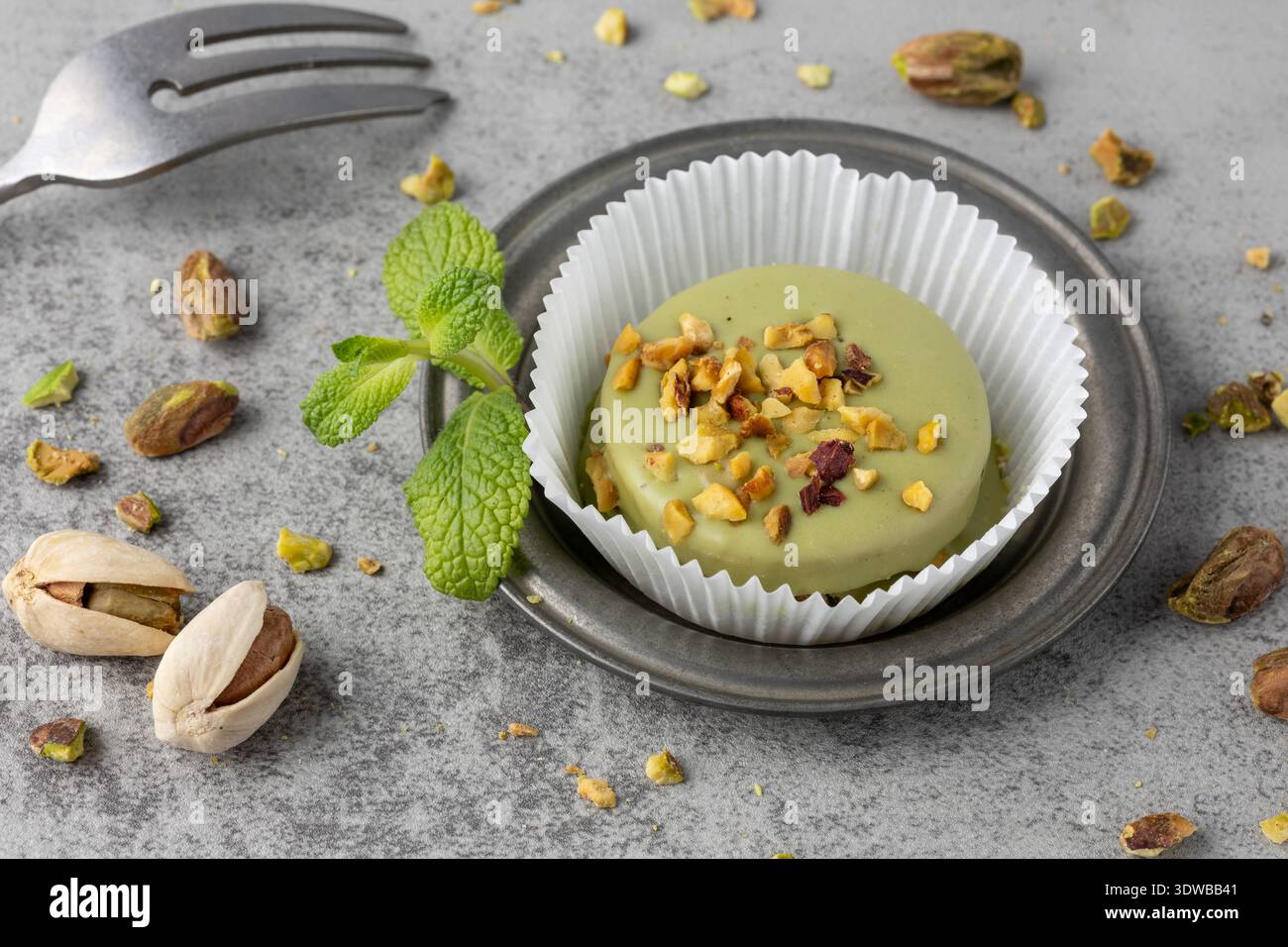 Grüner glasierter Mignonkuchen mit gerösteten Pistazien und Krümeln auf Retro-Platte auf grauem Steinhintergrund. Süßes Mignon-Gebäck-Dessert. Stockfoto