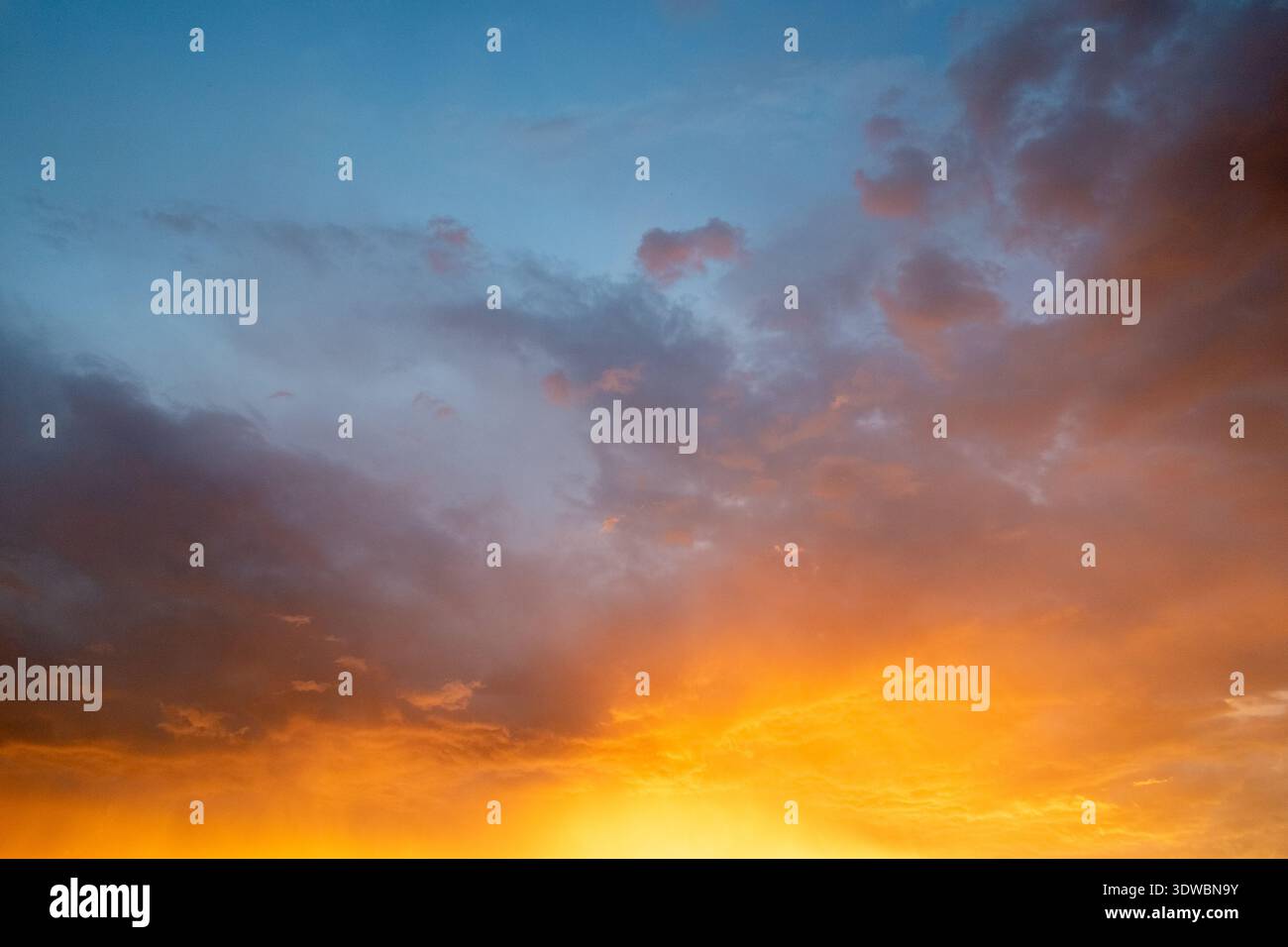 Eine lebendige Naturaufnahme eines dramatischen Wolkenhimmels, der bei Sonnenuntergang oder Sonnenaufgang von tiefem Blau zu leuchtendem Orange wechselt. Stockfoto