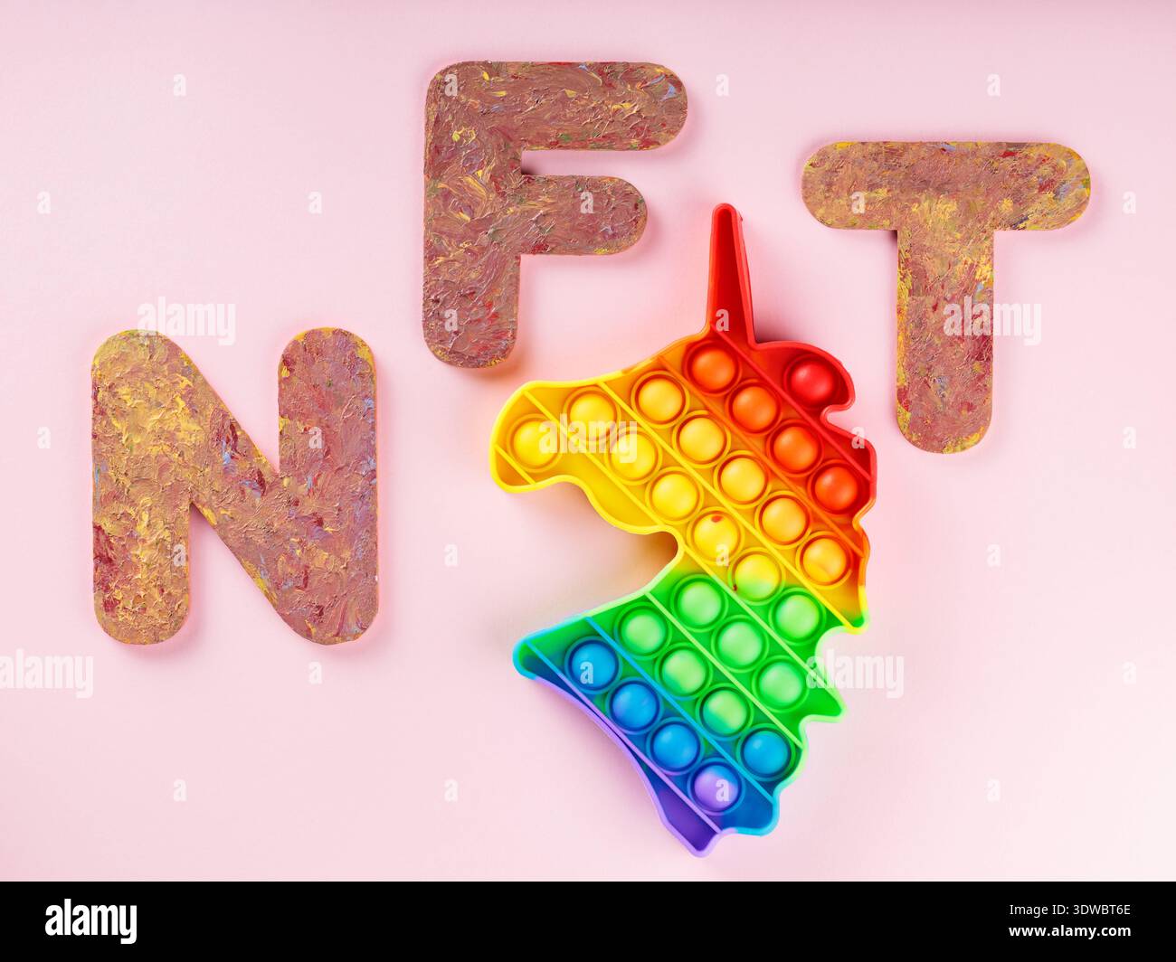 Buntes Spielzeug mit Regenbogenverlauf und NFT-Buchstaben auf rosafarbenem Hintergrund für Stressabbau Stockfoto