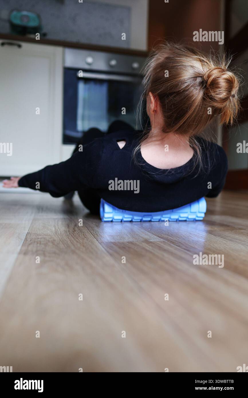 Rückansicht einer Frau, die sich auf einer Schaumwalze spannt. Körperpflege, Rehabilitationsübung und Wellness-Routine Stockfoto