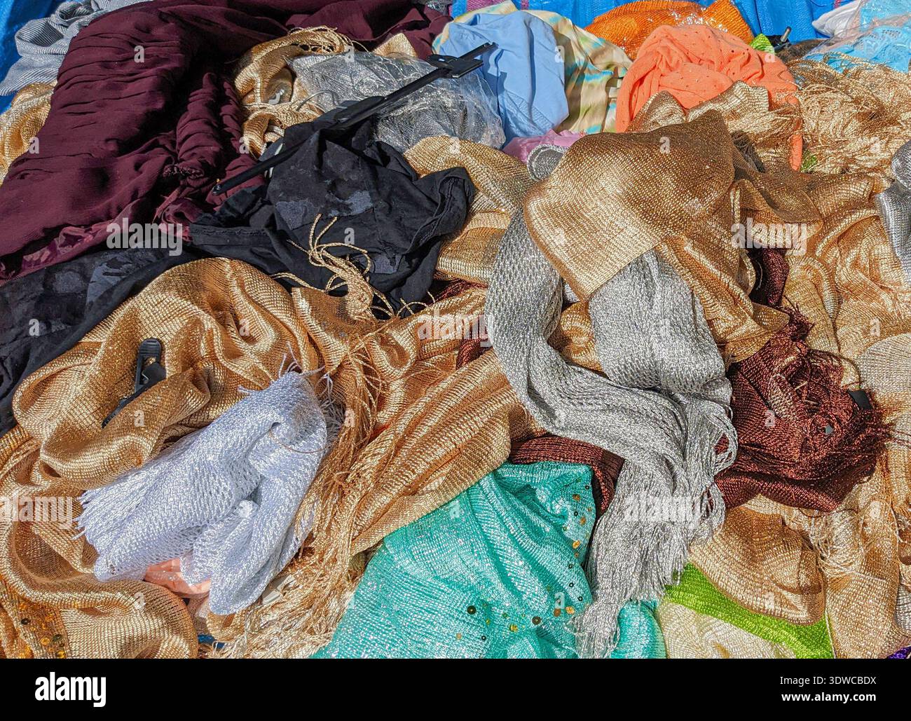 Ein Haufen glänzender Webstoffe in Gold-, Silber-, Türkis-, Schwarz- und Burgundertönen, sichtbare Metallfäden und Netzstrukturen, gefaltet und zerknittert Stockfoto