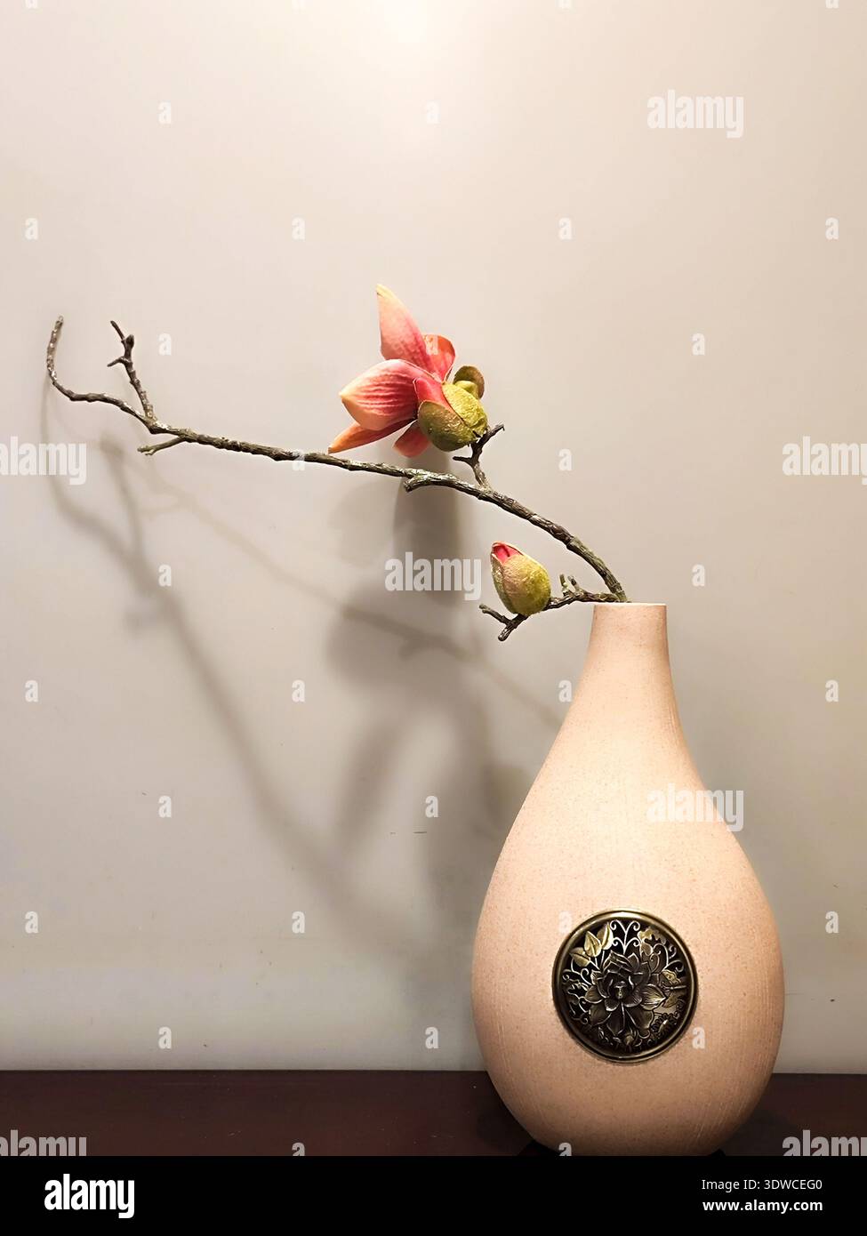 Ein einzelner Zweig mit einer blühenden Blume, die künstlerisch in einer minimalistischen Keramikvase vor einer sauberen weißen Wand platziert ist und die Zen-Ästhetik unterstreicht. Stockfoto