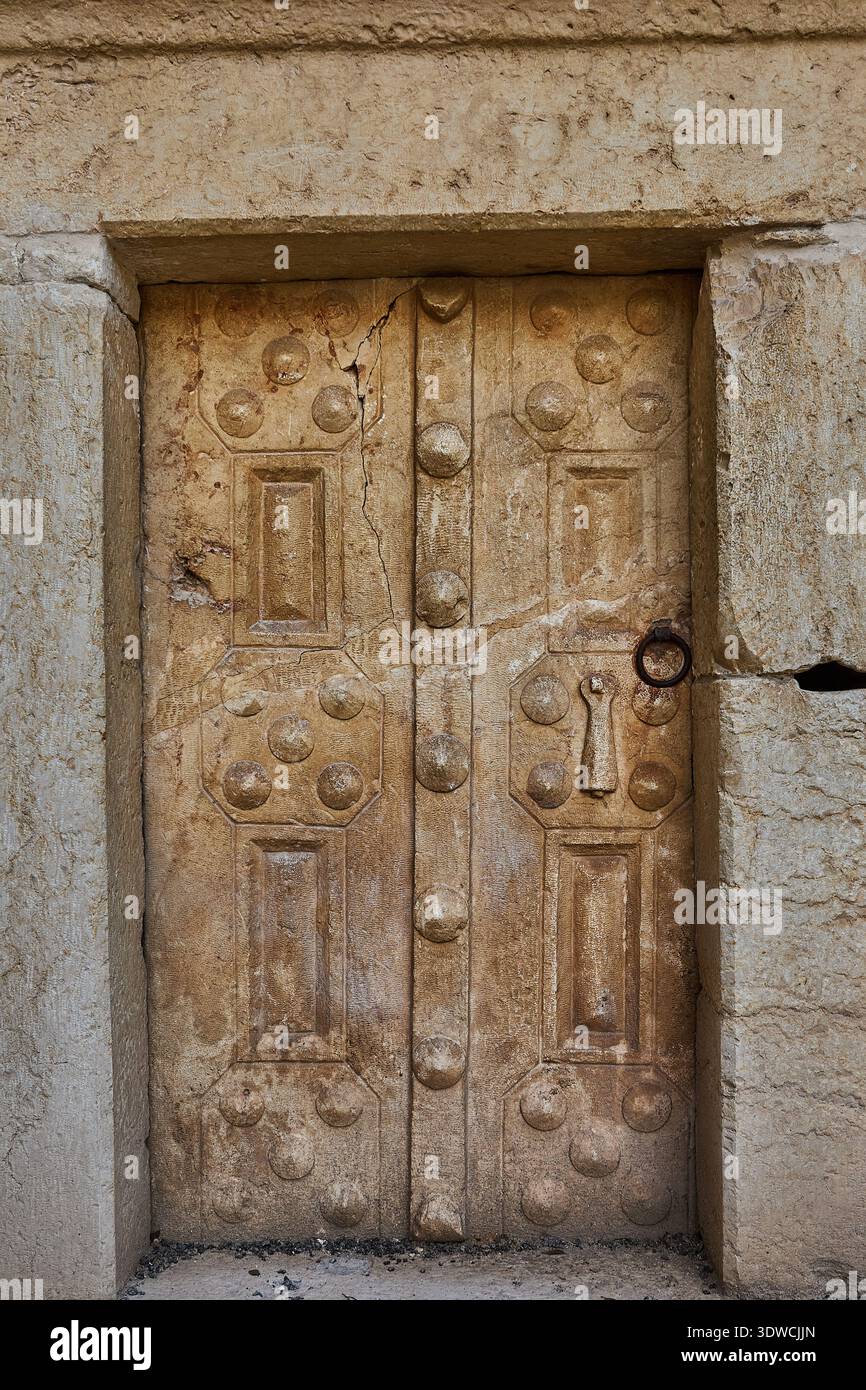 Alte Steintür mit dekorativen Schnitzereien und Metallgriff, in einer verwitterten Steinmauer, die historische architektonische Merkmale von A zeigt Stockfoto