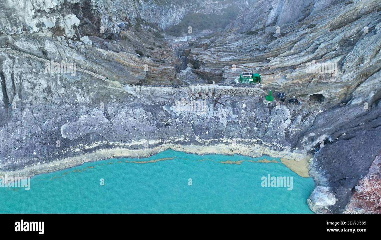Aus der Vogelperspektive auf die Felsenklippe am Kawah Ijen Vulkan mit türkisfarbenem Schwefelwassersee bei Sonnenaufgang. Fantastischer Blick auf die Naturlandschaft in Ost-Java, Indonesien. Natu Stockfoto