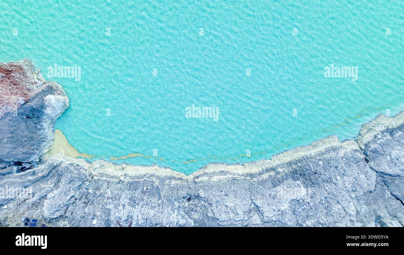 Türkisfarbenes Wasser des Kawah Ijen Acid Lake wirbelt unter zerklüfteten Kraterwänden und schwimmenden Schwefelwolken und erzeugt einen eindringlich schönen vulkanischen Amphit Stockfoto