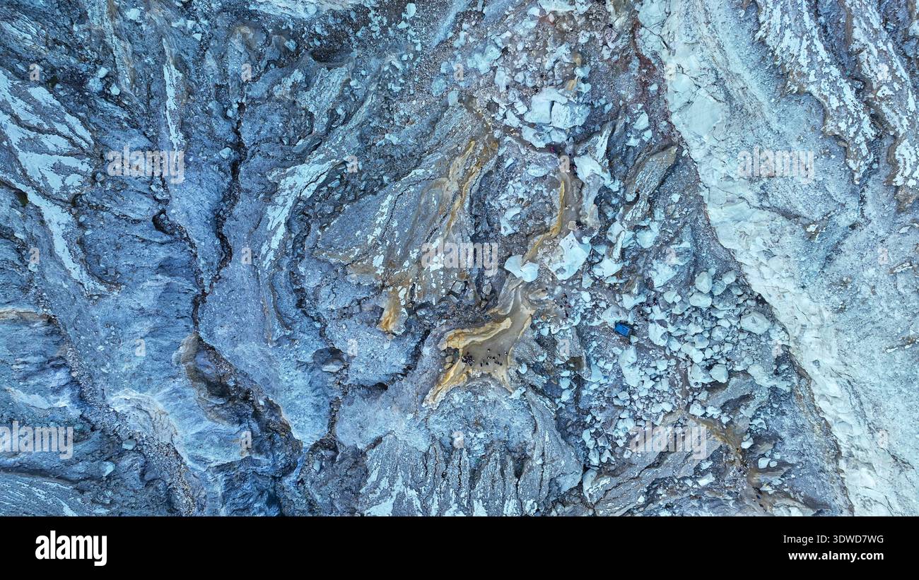 Nahaufnahme der zerklüfteten Kraterfelsen von Kawah Ijen. Goldene Adern aus Mineralablagerungen erstrahlen gegen das leuchtende Blau und zeigen den anderen Vulkan Stockfoto