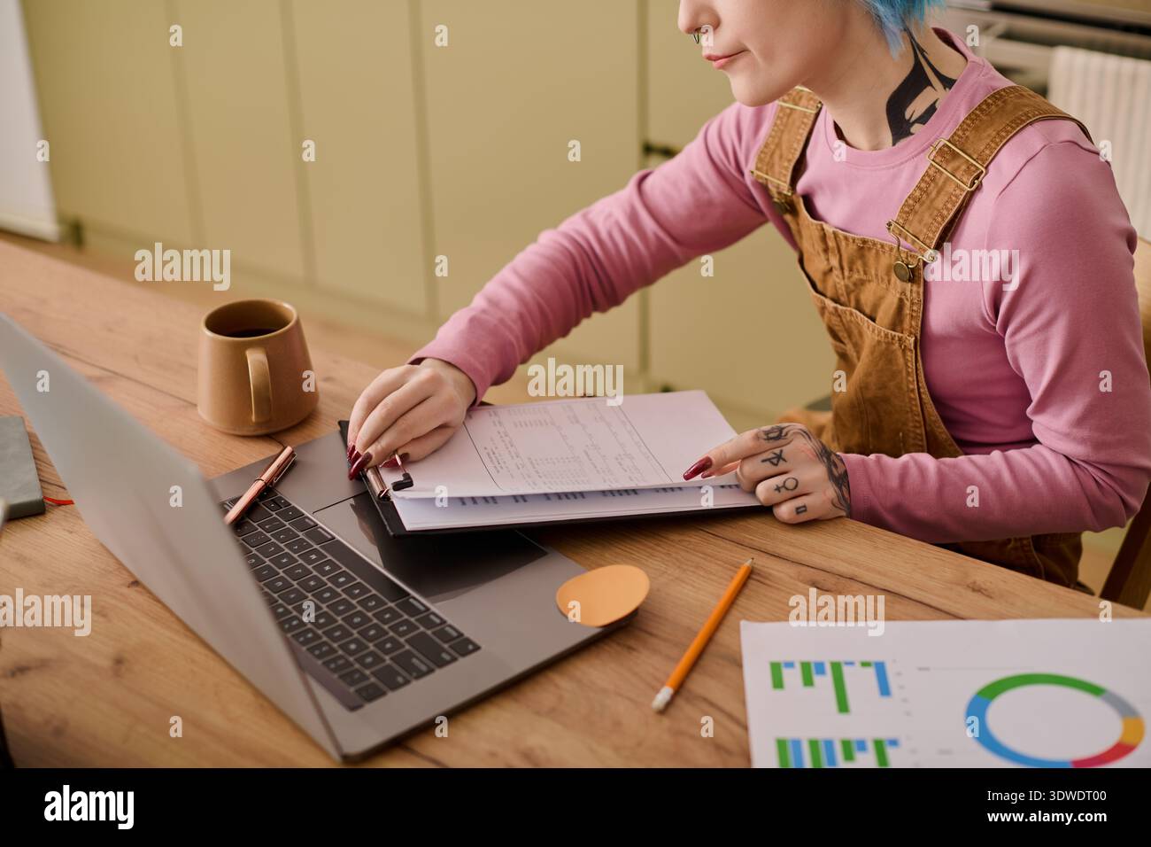 Eine lebendige junge Frau konzentriert sich auf ihre Projekte an einem Holztisch mit Notizen und einem Laptop. Stockfoto