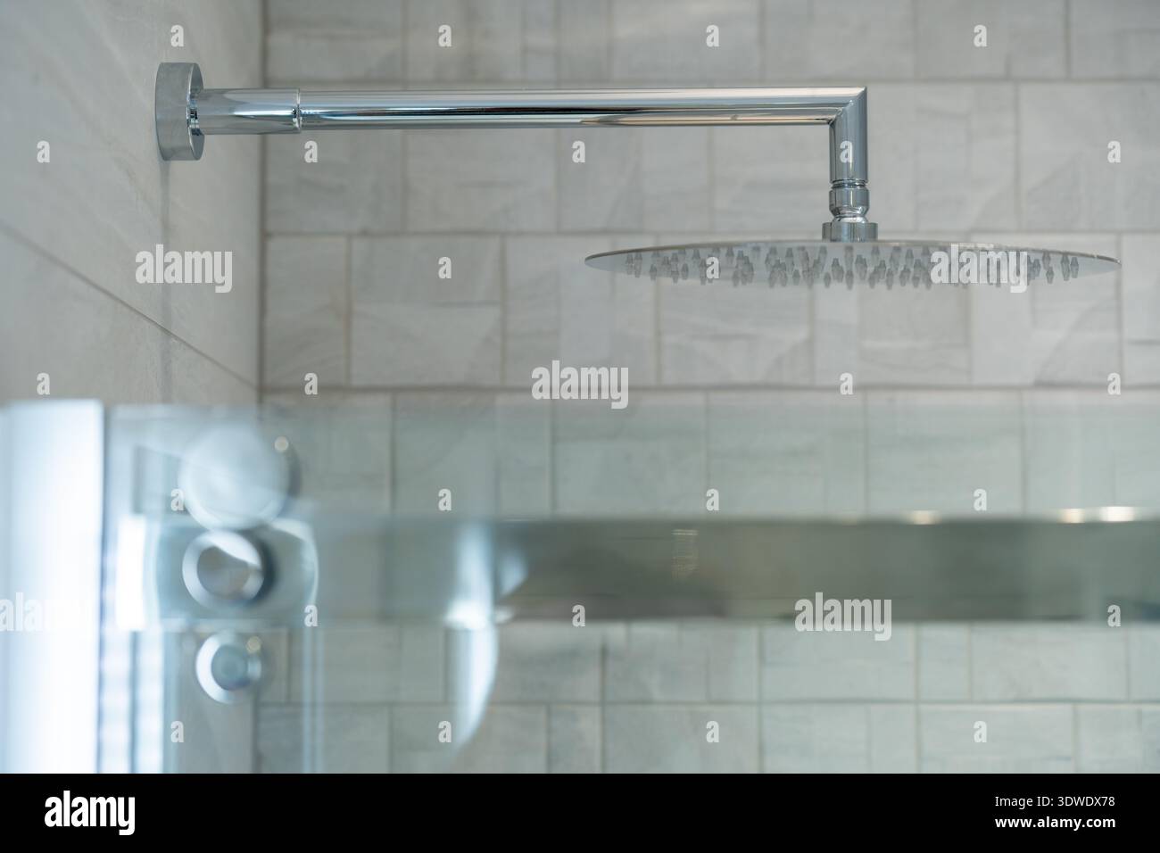 Moderner Duschkopf in einem stilvollen Londoner Badezimmer mit strukturierten grauen Fliesen und einer eleganten Glastür. Das minimalistische Design verbessert die Ästhetik und Stockfoto