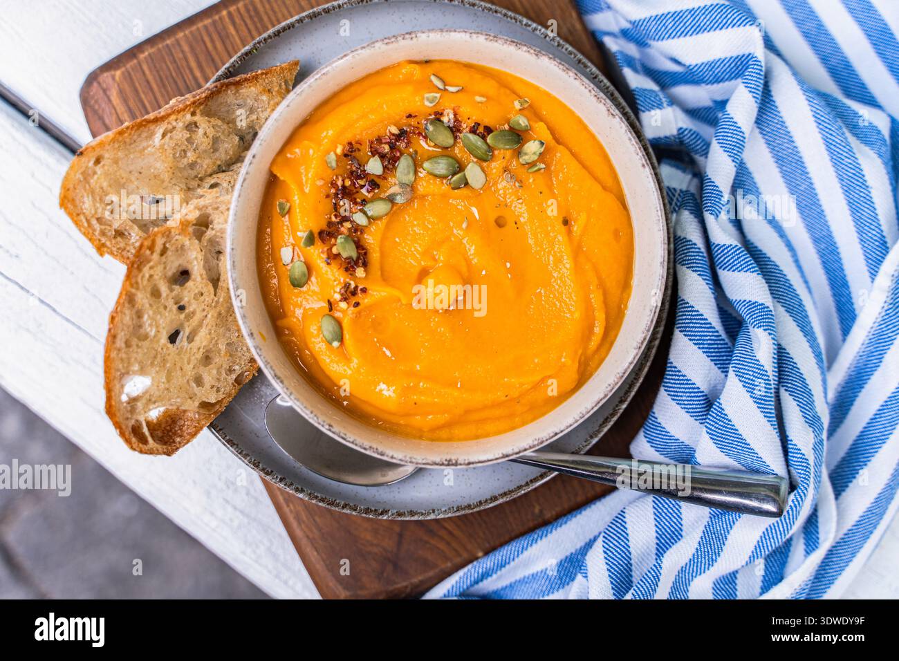 Eine köstliche Schüssel mit cremiger Kürbissuppe garniert mit Samen, serviert zusammen mit rustikalen Brotscheiben. Dieses herbstliche Gericht bietet Wärme und Komfort Stockfoto