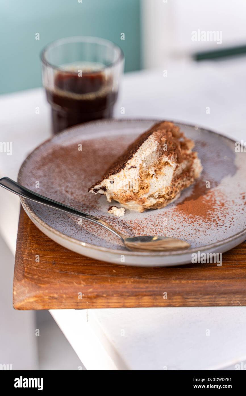 Eine köstliche Scheibe Tiramisu sitzt einladend auf einer Keramikplatte, kombiniert mit einer reichhaltigen, aromatischen Tasse Kaffee. Dieses klassische italienische Dessert ist wunderschön Stockfoto