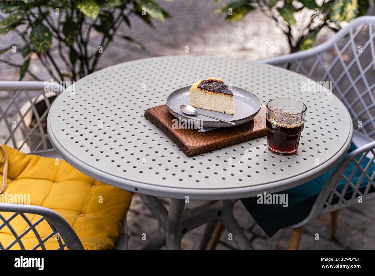 Ein köstliches Stück baskischen Käsekuchen serviert auf einem dekorativen Tisch im Freien, begleitet von einer erfrischenden Tasse Kaffee. Die perfekte Dessertpaarung für Stockfoto