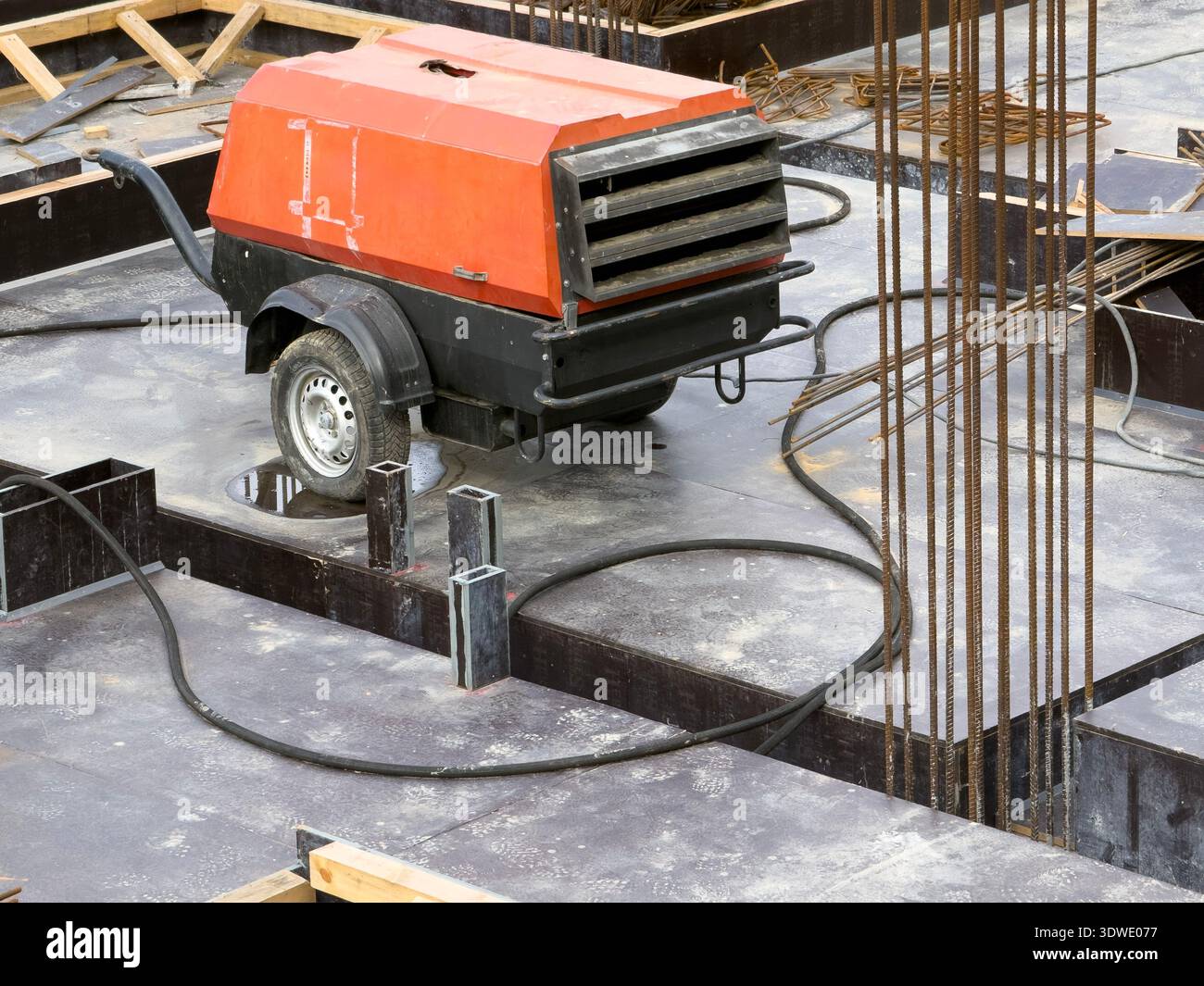Eine tragbare Kompressormaschine auf einer Baustelle, umgeben von Baumaterialien und Werkzeugen. Unverzichtbar für verschiedene Konstruktionen Stockfoto