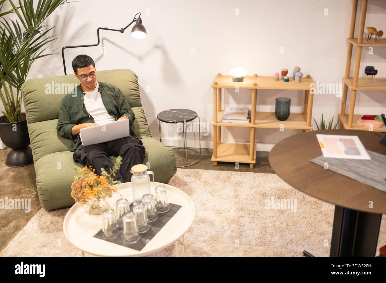 Ein komfortables Coworking-Büro mit teamfreundlichem Ambiente und modernen Möbeln. Ein Mann arbeitet an einem Laptop und genießt eine entspannte Stockfoto