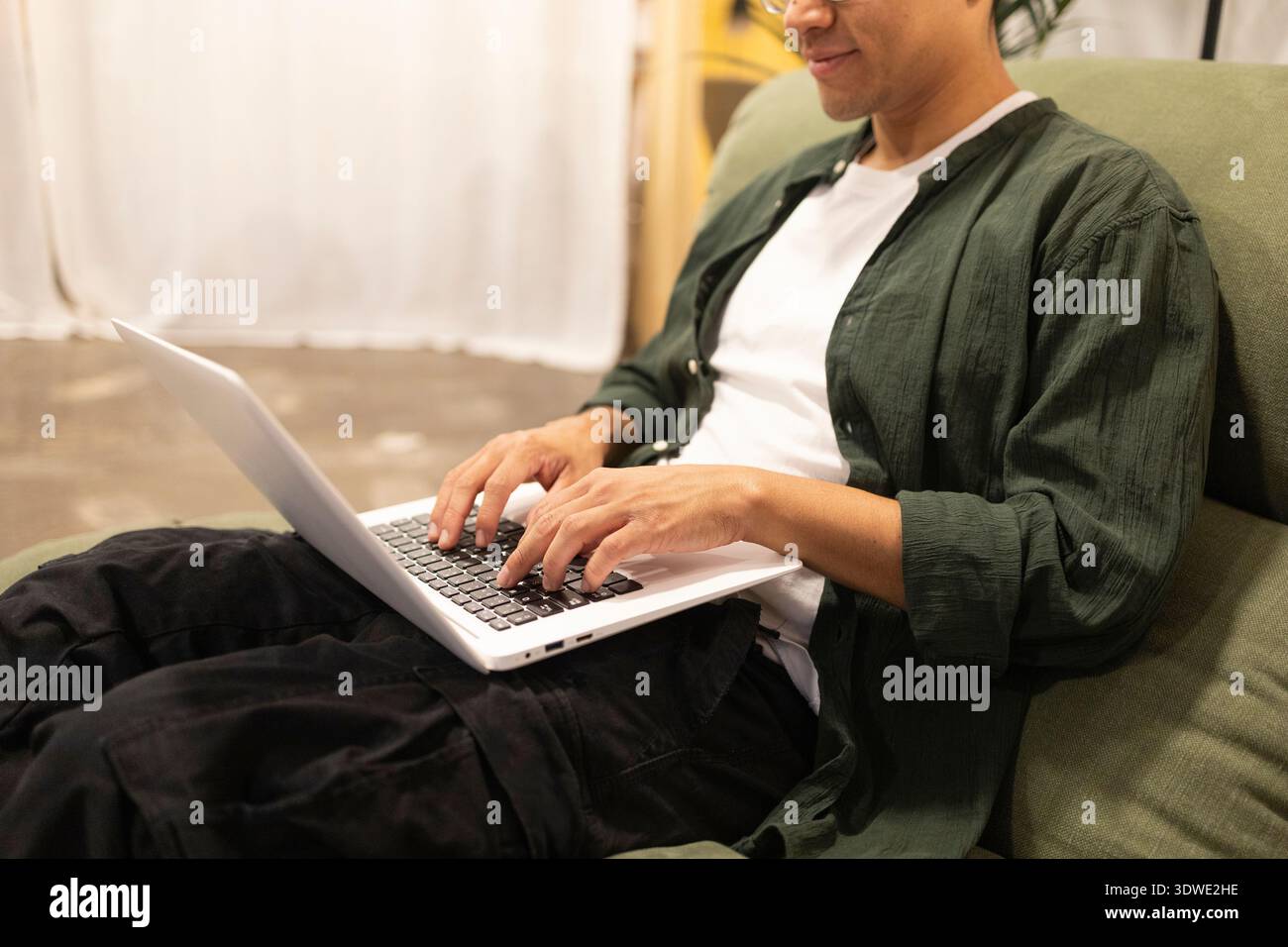Ein Mann arbeitet an einem Laptop in einem zwanglosen Coworking-Raum und unterstreicht eine entspannte Büroumgebung. Der Schwerpunkt liegt auf Zusammenarbeit und Produktivität in Stockfoto