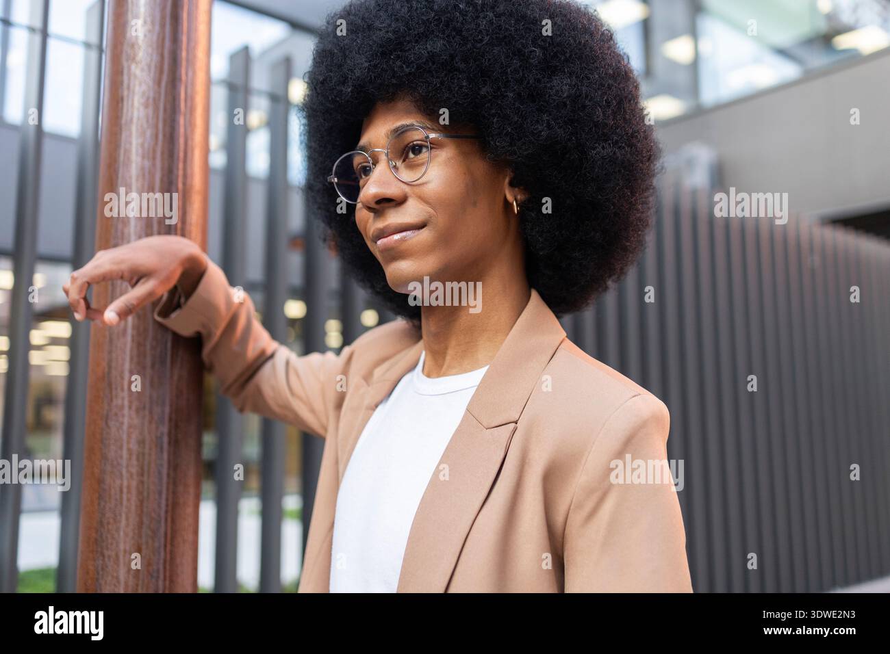 Ein selbstbewusster Mensch in einer modernen Umgebung mit einem stilvollen braunen Blazer und einer Brille. Ihr legeres weißes Oberteil ergänzt den professionellen Look und strahlt M aus Stockfoto