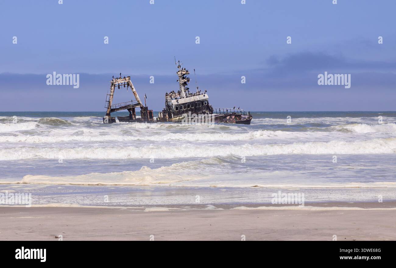 Ein rostendes Schiffswrack liegt teilweise unter Wasser entlang Namibias Skeleton Coast, ein Zeugnis für die Kraft der Natur. Die Wellen des Atlantiks stürzen dramatisch ab Stockfoto