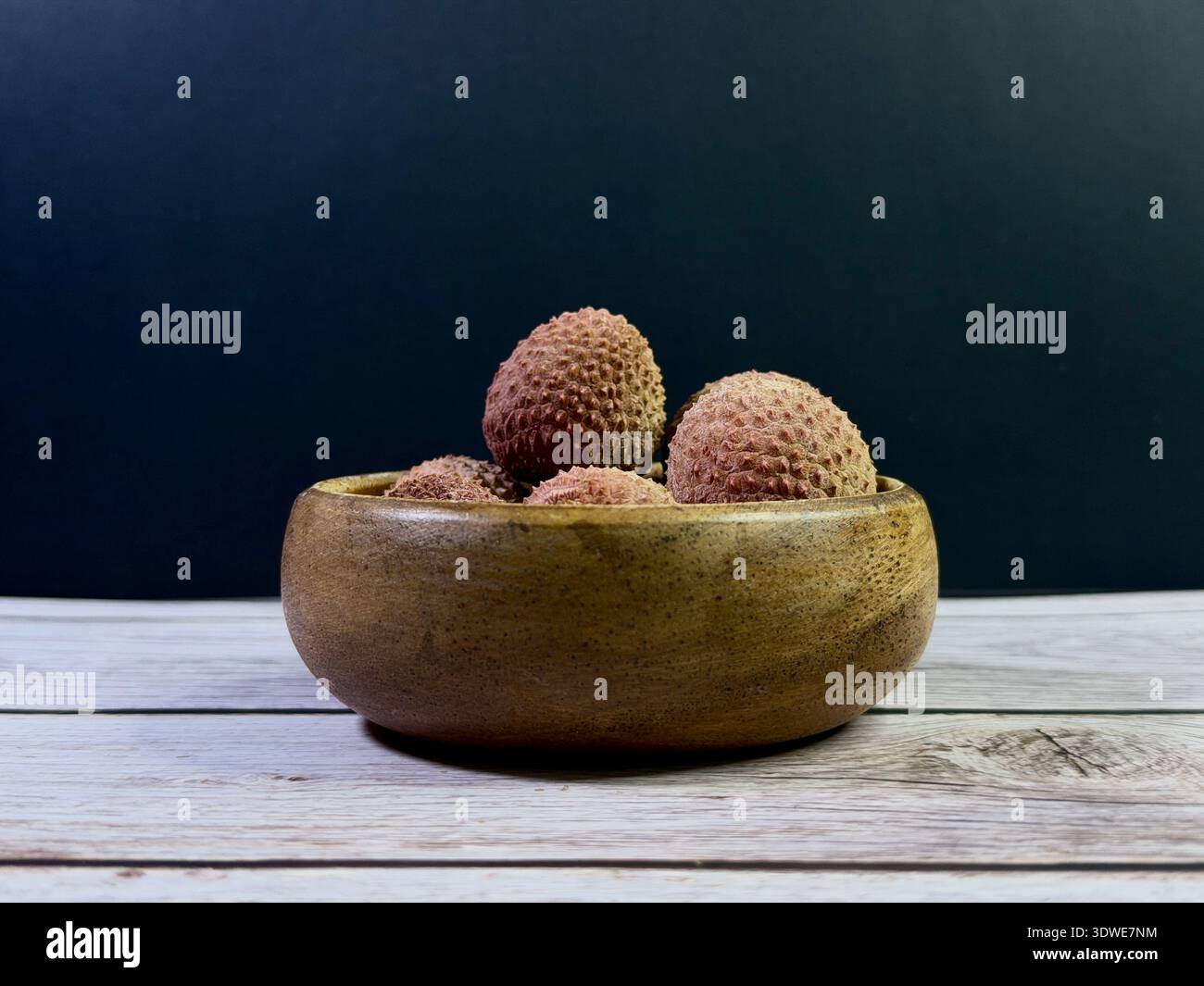 Frisches Litschi-Obst in einer rustikalen Holzschale auf einem Holztisch. Natürliche Bio-Lebensmittel Stillleben mit warmen Tönen und Bauernküche Ästhetik. - Smartphone-aufgenommenes Stockfoto