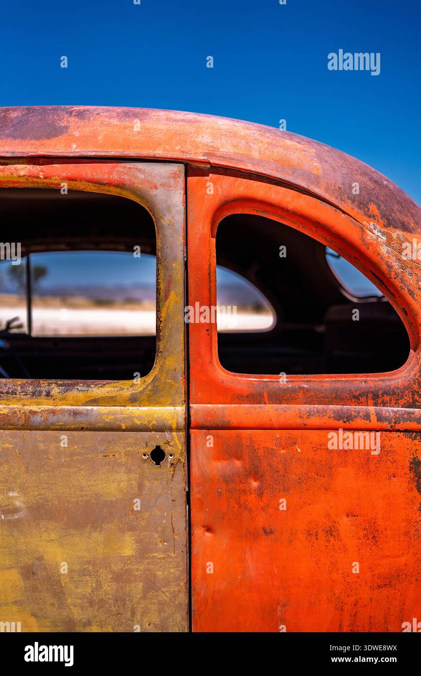 Eine detaillierte Nahaufnahme einer rustikalen Oldtimertür mit verwitterter orange-gelber Farbe unter einem klaren blauen Himmel. Die abgenutzte Struktur erfasst ein Stockfoto