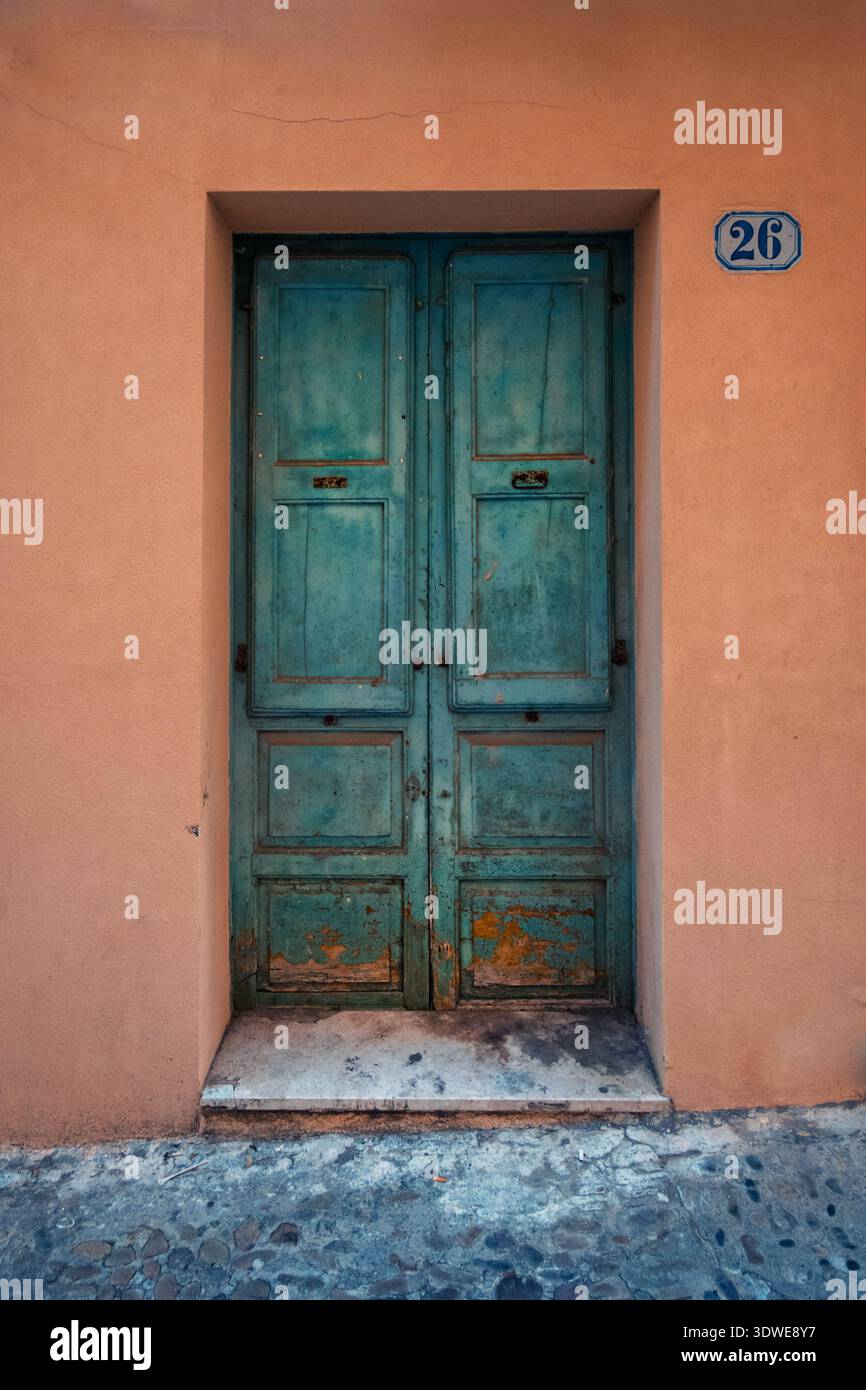 Eine wunderschön verwitterte türkisfarbene Tür ziert eine rustikale pfirsichfarbene Wand in Cefalu, Sizilien. Die einzigartige Farbe der Tür bildet einen bezaubernden Kontrast zum Surro Stockfoto