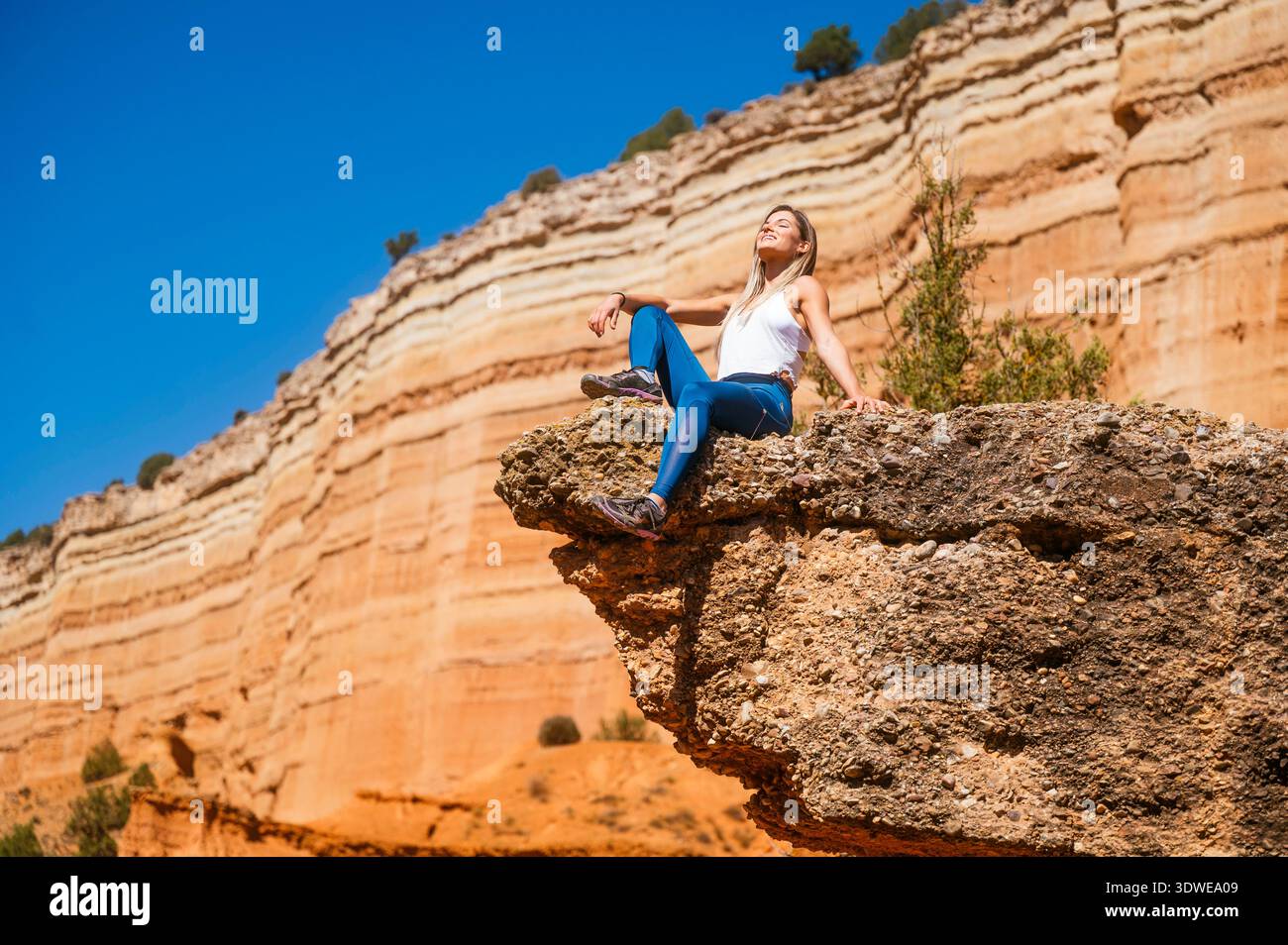 Eine Frau genießt ein aufregendes Abenteuer im Red Canyon. Sie entspannt sich auf einem felsigen Felsvorsprung vor der majestätischen Kulisse der mehrschichtigen Canyonwände, wo sie sich in sich ergossen Stockfoto
