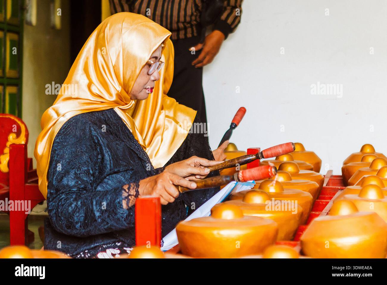 Eine Frau in goldenem Hijab und traditioneller Kleidung spielt das Gamelan, ein traditionelles javanisches Musikinstrument, das sich intensiv auf die Gestaltung von M konzentriert Stockfoto
