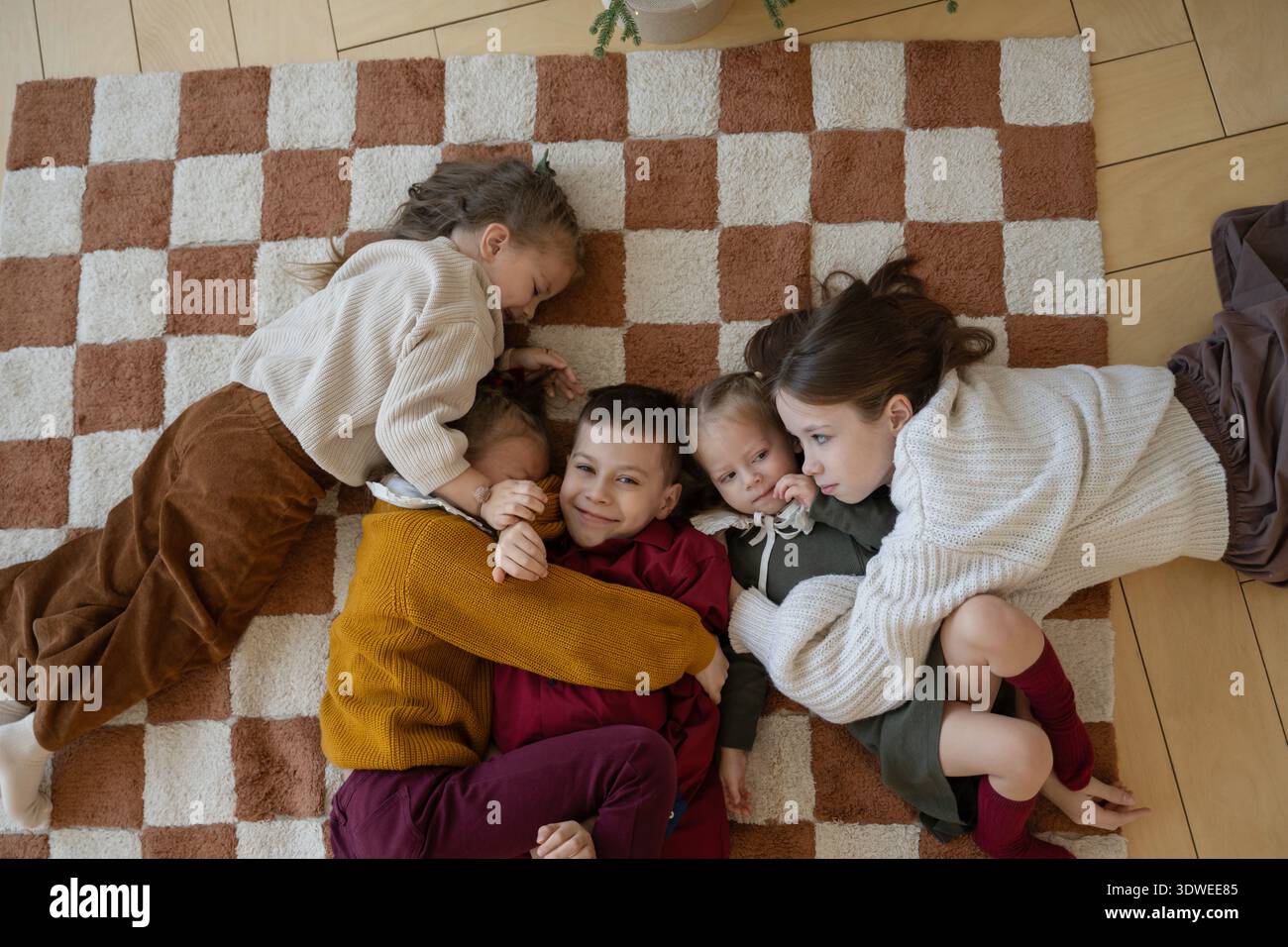 Eine herzerwärmende Weihnachtsszene mit Kindern, die sich auf einen weichen, karierten Teppich kuscheln und die Freude und Wärme der Weihnachtszeit mit einem Lächeln feiern Stockfoto