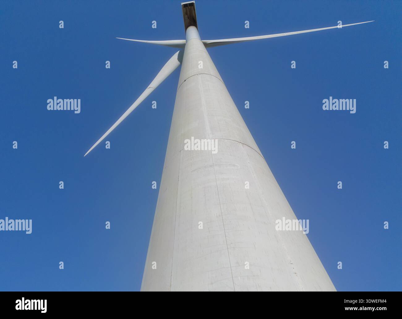 Luftaufnahme der hoch aufragenden Windkraftanlage, die sich bis zum azurblauen Himmel erstreckt, mit ihren Rotorblättern gegen den Horizont, Teba, Andalusien, Spanien. Stockfoto