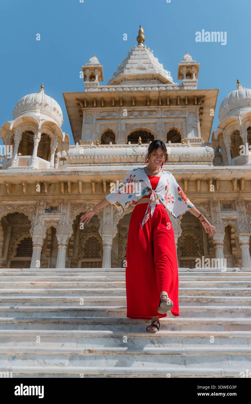 Eine fröhliche Frau in leuchtend roter Kleidung steigt anmutig die Stufen eines herrlichen Tempels in Indien hinab und fängt das Wesen der kulturellen Schönheit und ein Stockfoto
