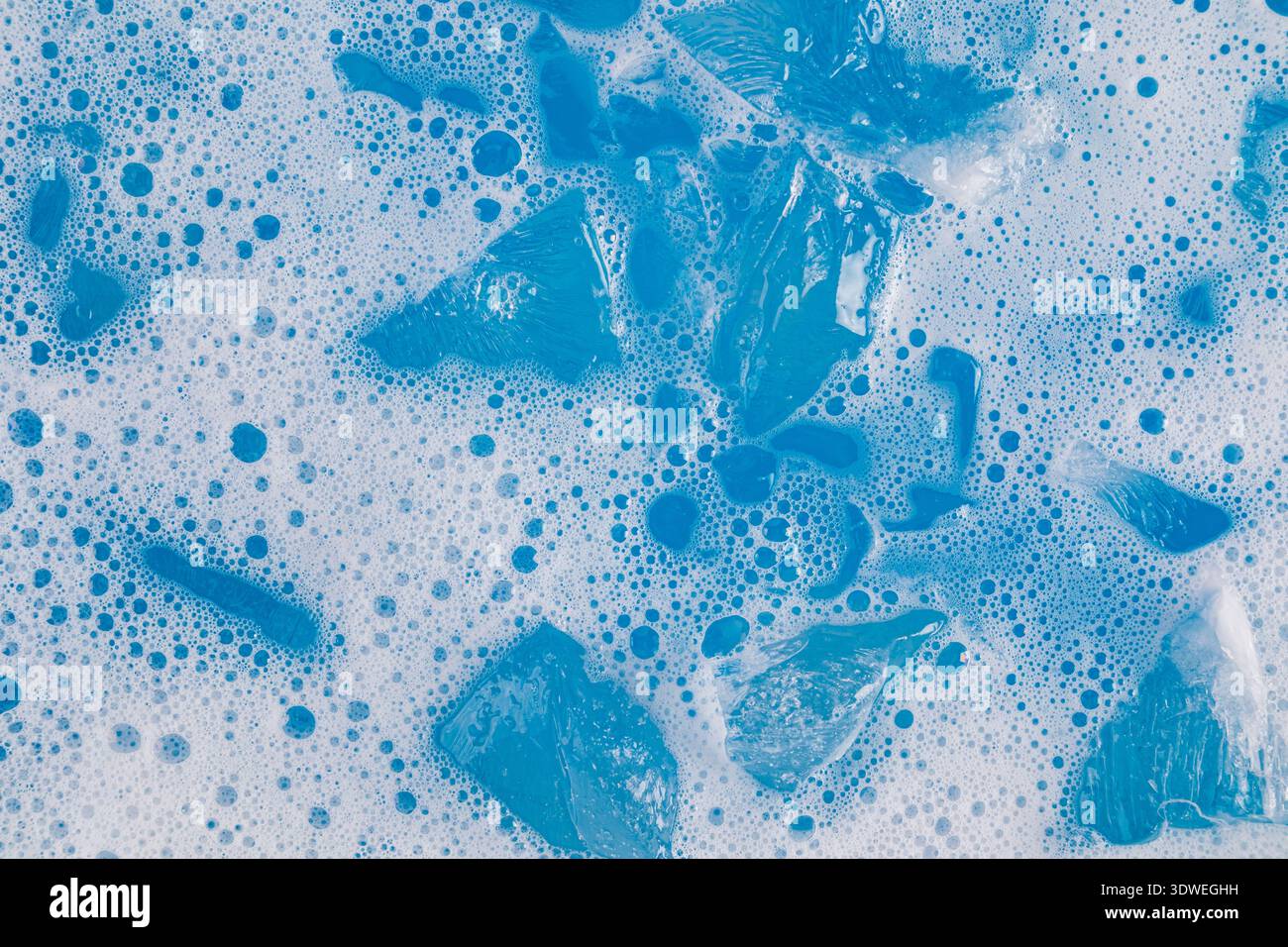 Eine erfrischende Szene mit Eiswürfeln, die in einem schaumigen, leuchtend blauen Matcha schweben. Der kühle Kontrast des Eises und die ausgelassenen Blasen sorgen für eine belebende Atmosphäre Stockfoto