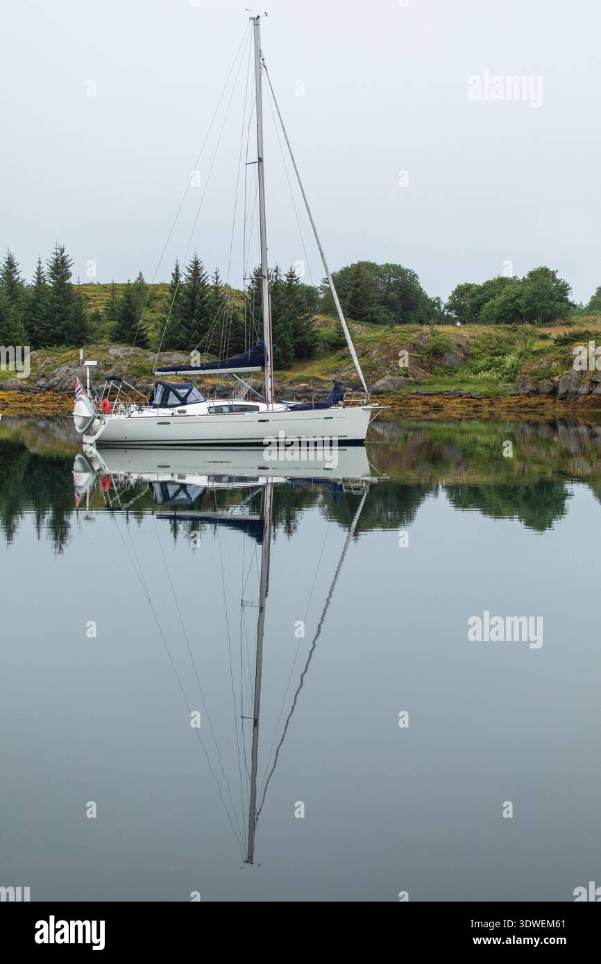Ein elegantes Segelboot liegt auf ruhigen norwegischen Gewässern und spiegelt die ruhige Landschaft wider. Umgeben von üppigem Grün, verkörpert es Ruhe Stockfoto