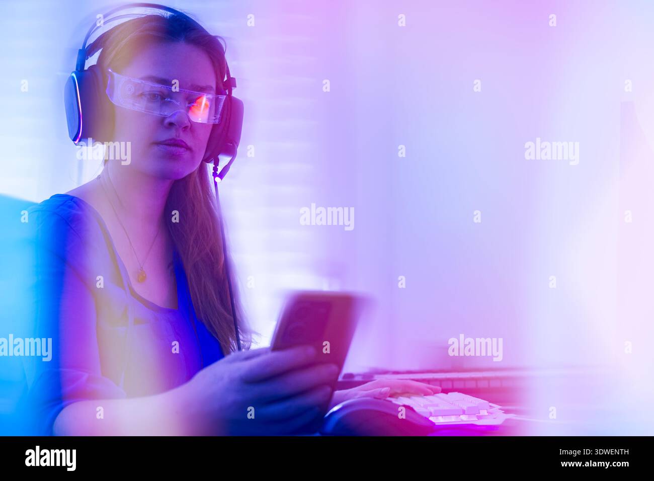 Eine Frau mit Kopfhörern und Brillen in einem Cyber-Ambiente. Der lebhafte Bokeh-Hintergrund in blau und rot sorgt für eine futuristische und Stockfoto