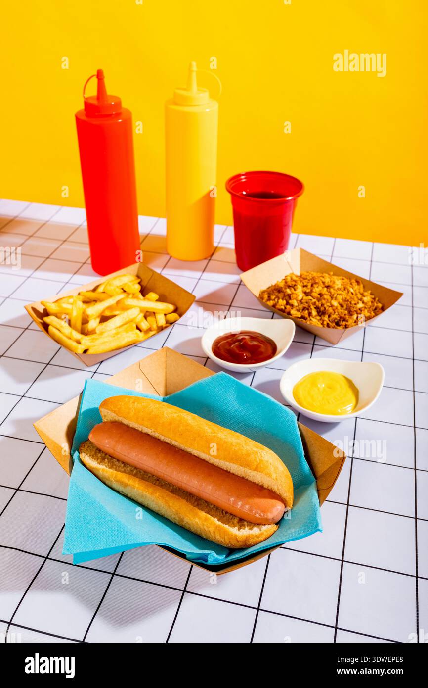Ein verführerischer Hot Dog in einem Brötchen, umgeben von knusprigen Pommes, Ketchup, Senf und einem leuchtend gelben Hintergrund, der das Wesen eines Genusses fängt Stockfoto