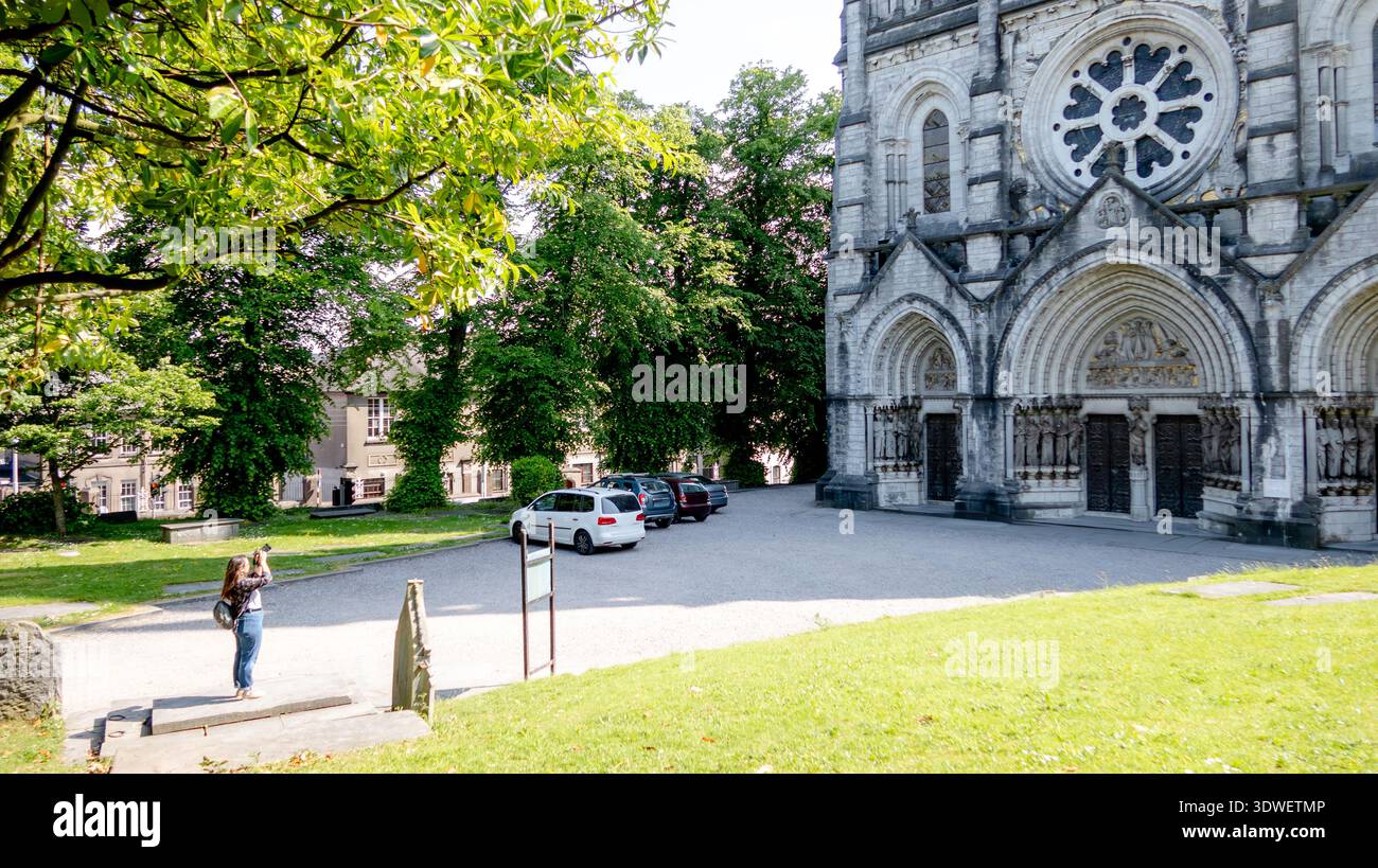 Ein Tourist fotografiert die Kathedrale Saint Fin Barre in Cork, Irland, an einem sonnigen Tag. Die gotische Architektur steht elegant vor der Kulisse des Lus Stockfoto