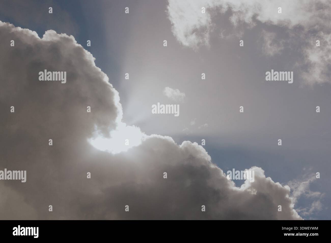 Sonnenlicht strömt durch dicke, dramatische Wolken in einem dynamischen Himmel, strahlt Strahlen aus und erzeugt ein markantes Licht- und Schattenspiel auf einem friedlichen, hellen Raum Stockfoto