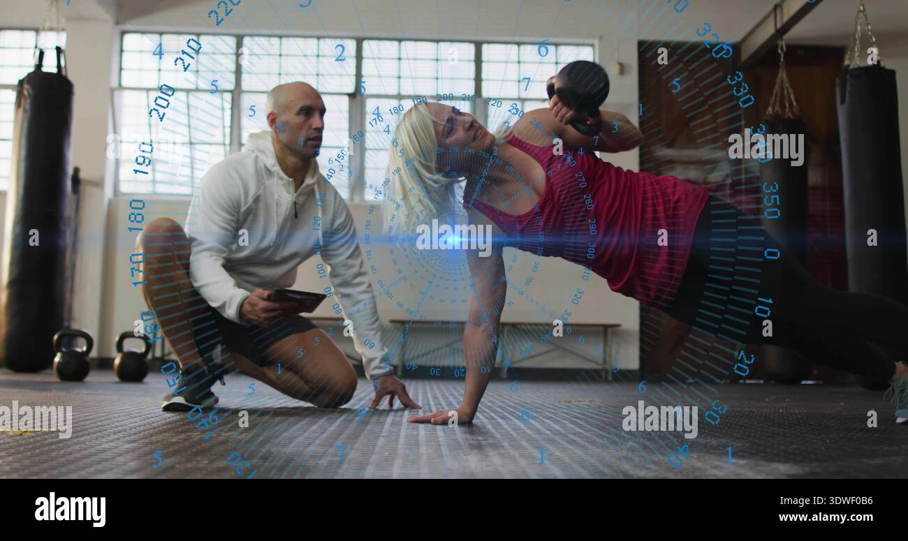 Die darstellende Frau hält eine Hantel an einer Hand in der roten Spitze des Fitnessstudios, Trainer notiert Tablet HUD Stockfoto