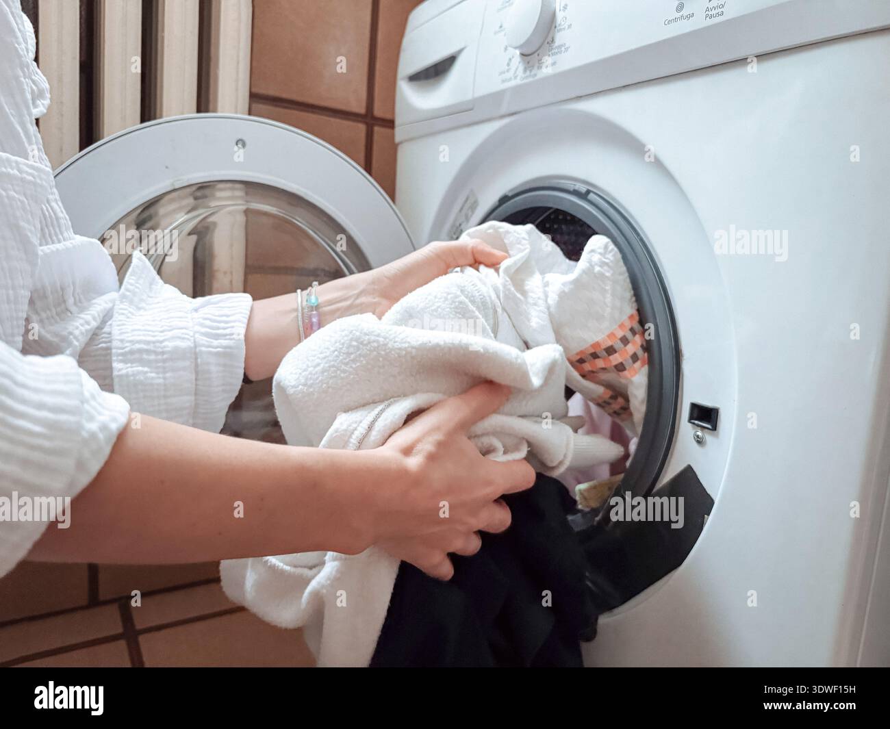 Eine Person lädt Kleidung in eine Waschmaschine und verkörpert die tägliche Routine einer morgendlichen Arbeit. Das Bild zeigt ein Gefühl von Frische und Ordnung Stockfoto